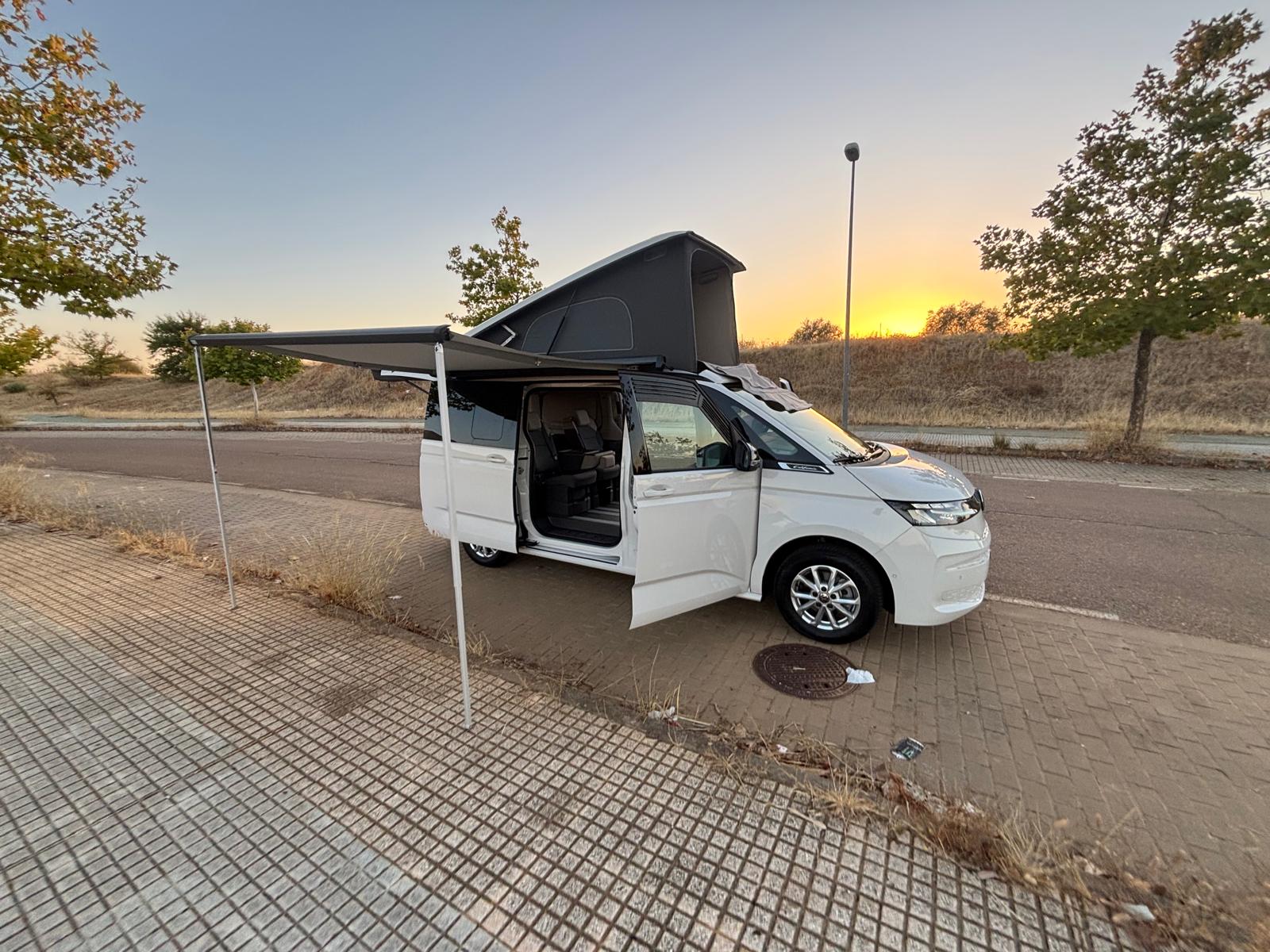 California con techo elevable, toldo desplegado y puerta corredera abierta al atardecer
